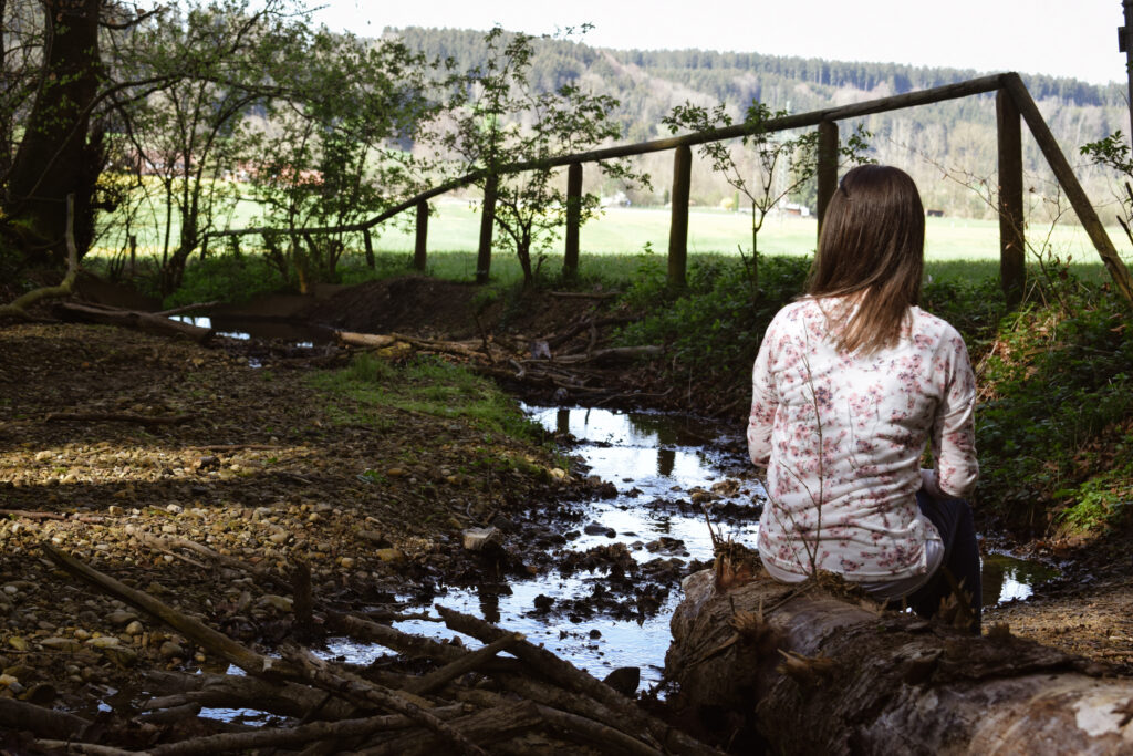 Frau sitzt an Wasserlauf